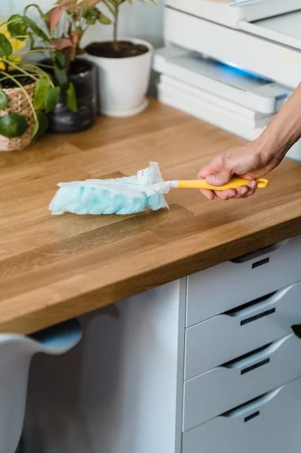 Personne anonyme portant des gants en caoutchouc jaunes et utilisant une simple éponge pour nettoyer un miroir dans une salle de bain